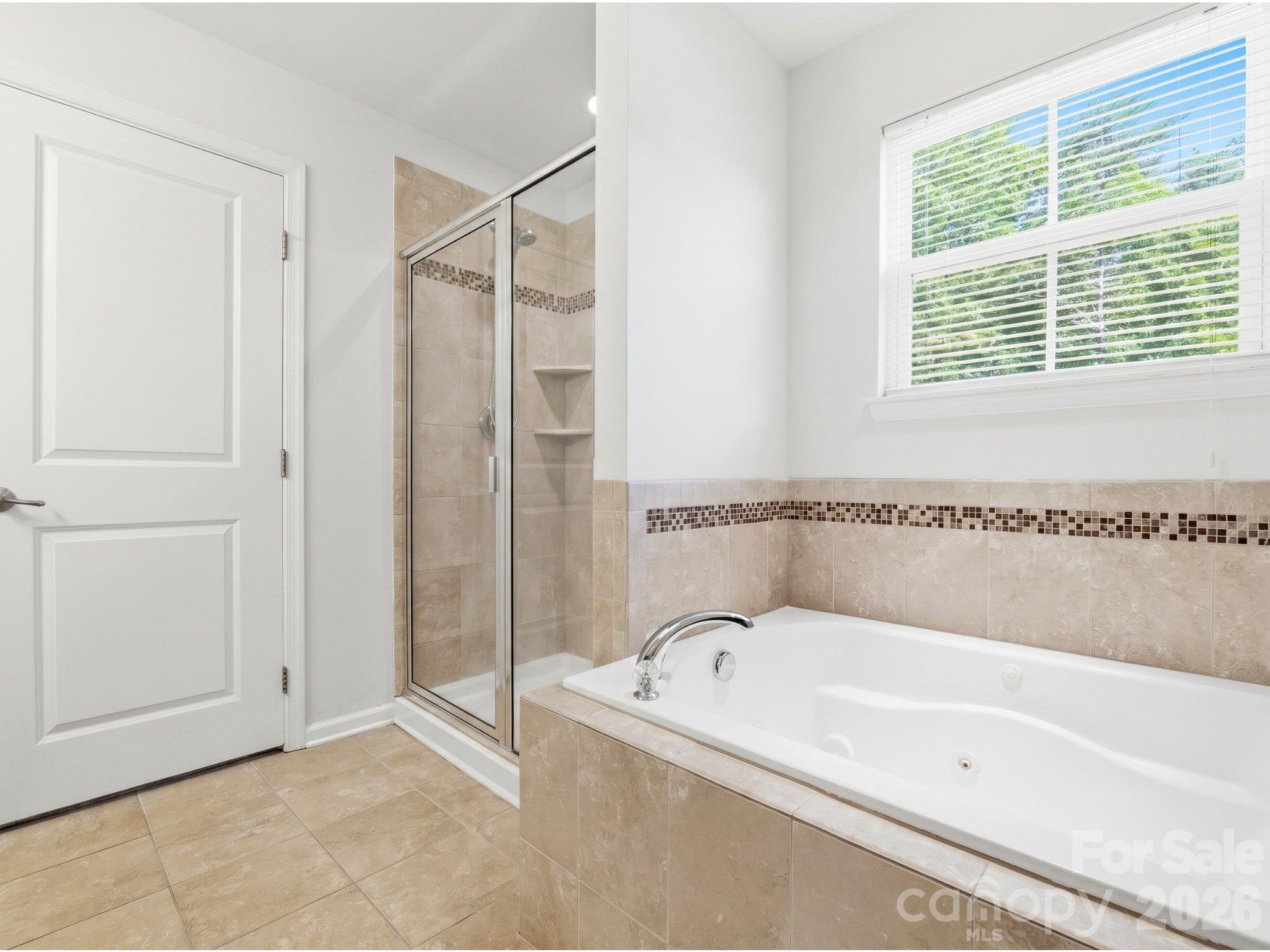 Primary ensuite: Jetted tub beneath a window, separate shower, and tile surround offer two bathing options. - 3341 Linetender Drive, Davidson