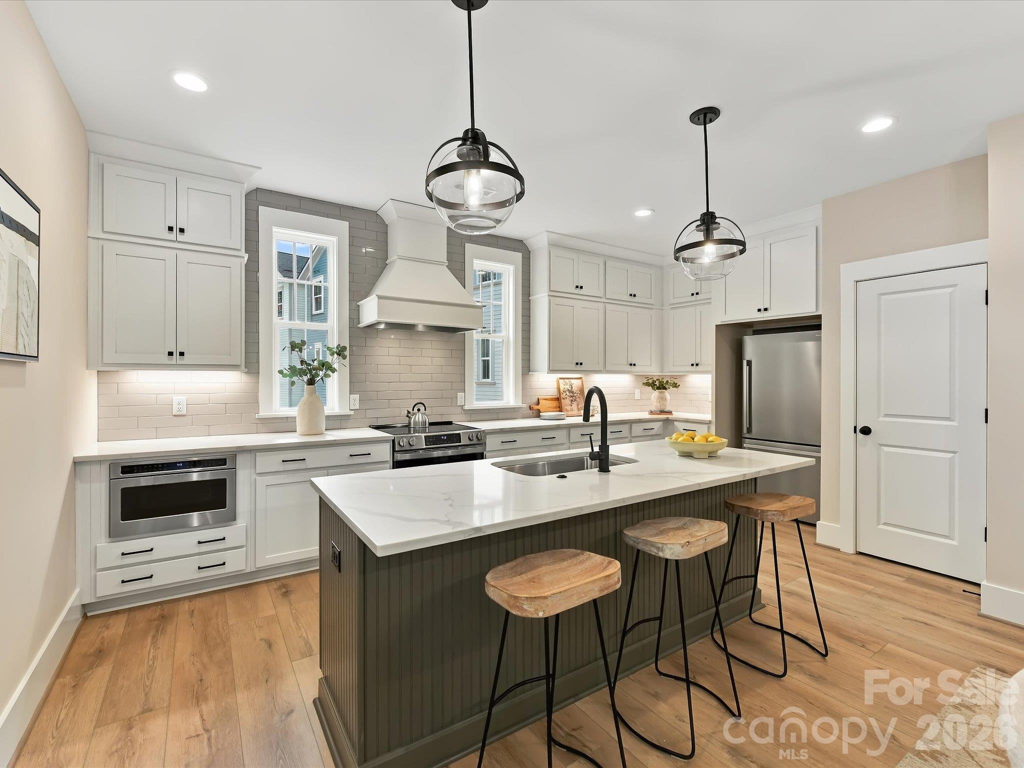 Beautifully appointed kitchen featuring modern white cabinetry, quartz-style countertops, stainless steel appliances, a spacious center island with breakfast bar seating, and stylish pendant lighting. - 225 Davidson Gateway Drive, Davidson