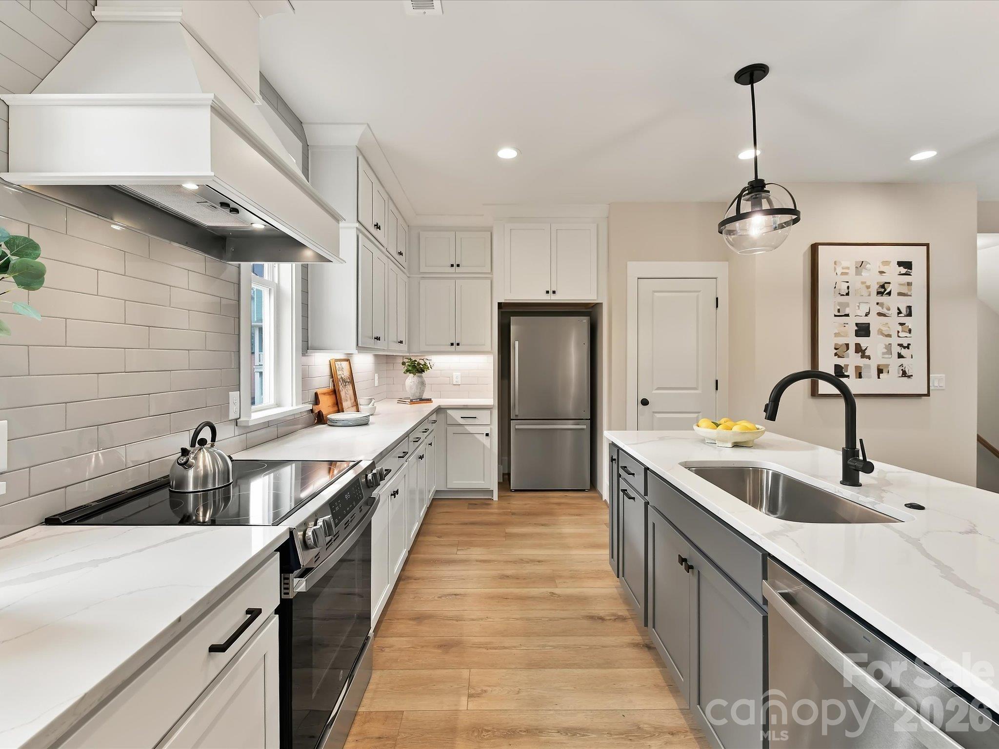 Beautifully appointed kitchen featuring modern white cabinetry, quartz-style countertops, stainless steel appliances, a spacious center island with breakfast bar seating, and stylish pendant lighting. - 225 Davidson Gateway Drive, Davidson