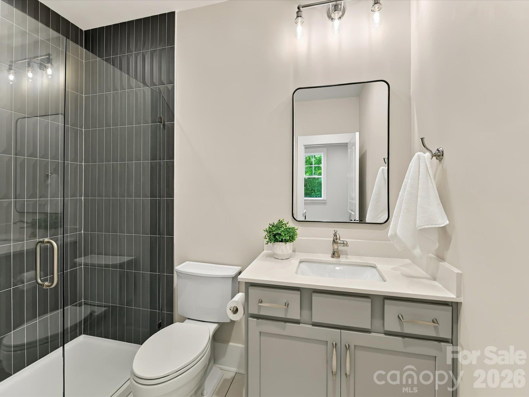 Modern full bath featuring a glass-enclosed shower with dark tile, a stylish vanity, sleek fixtures, and contemporary lighting. - 225 Davidson Gateway Drive, Davidson