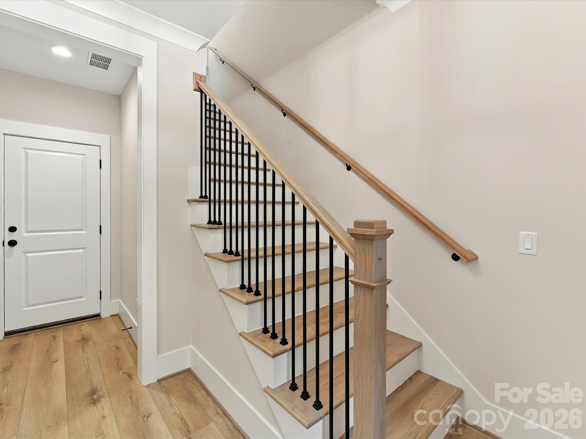 Stylish staircase featuring natural wood treads, sleek black metal balusters, and a coordinating wood handrail for a modern, elegant look. - 225 Davidson Gateway Drive, Davidson