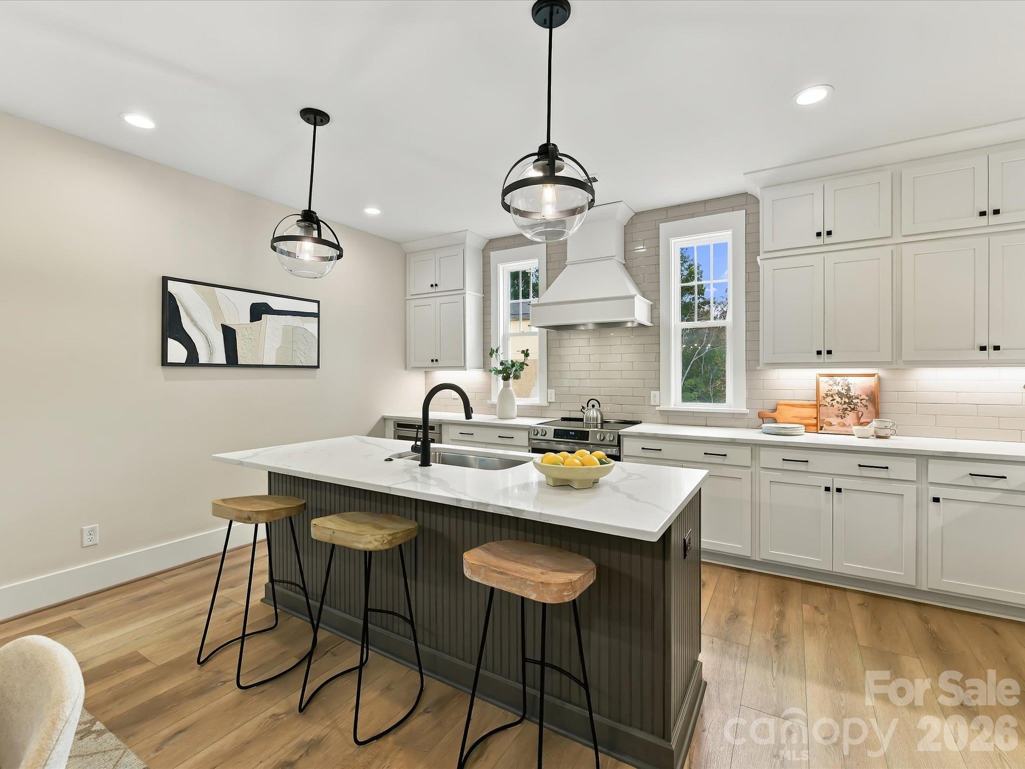 Beautifully designed kitchen featuring modern white cabinetry, quartz countertops, stainless steel appliances, a spacious center island with breakfast bar seating, and an open flow into the dining and living areas. - 225 Davidson Gateway Drive, Davidson