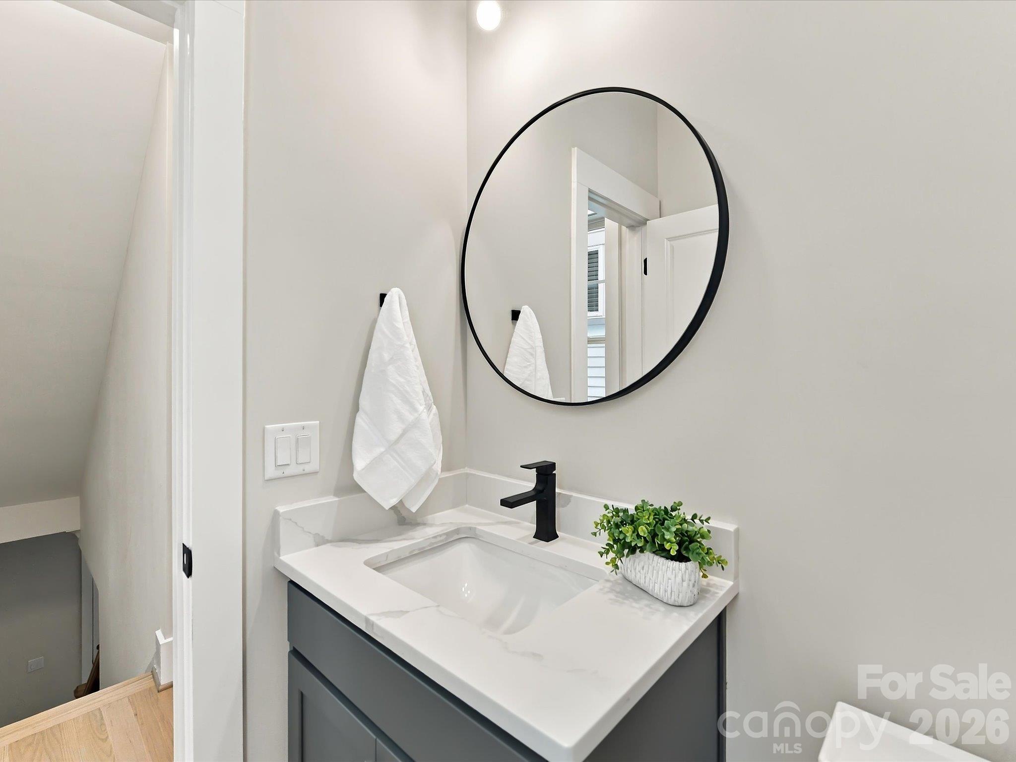 Stylish powder room featuring a modern gray vanity, marble-look countertop, matte black fixtures, and a sleek round mirror. - 225 Davidson Gateway Drive, Davidson