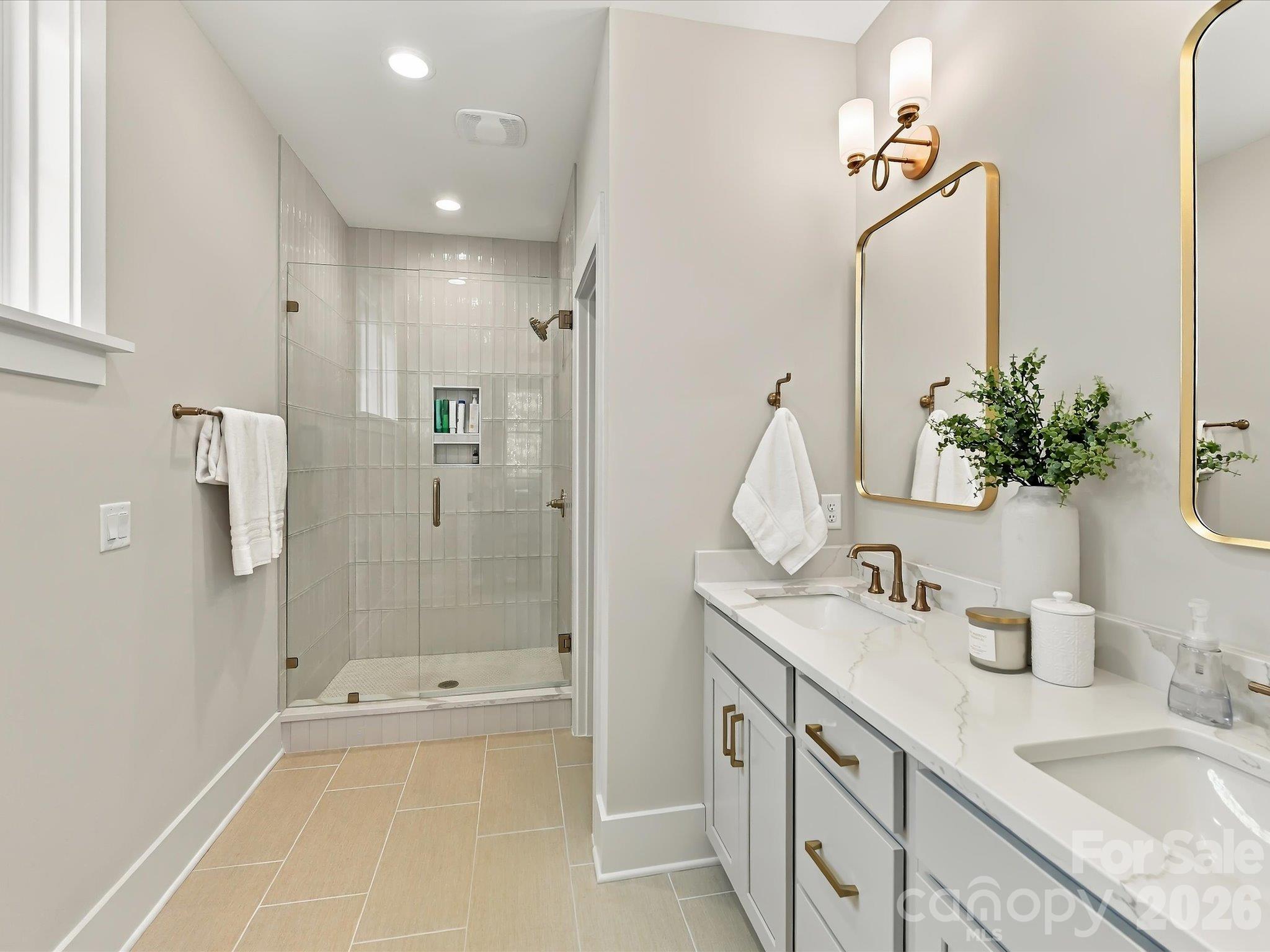 Elegant primary bath featuring a dual-sink vanity, quartz-look countertops, gold fixtures, and a spacious glass-enclosed shower with beautiful tilework. - 225 Davidson Gateway Drive, Davidson