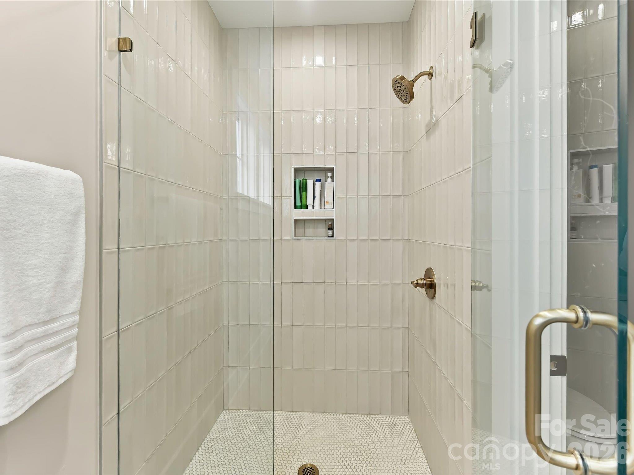 Elegant primary bath featuring a dual-sink vanity, gold fixtures, and a spacious glass-enclosed shower with beautiful tilework. - 225 Davidson Gateway Drive, Davidson