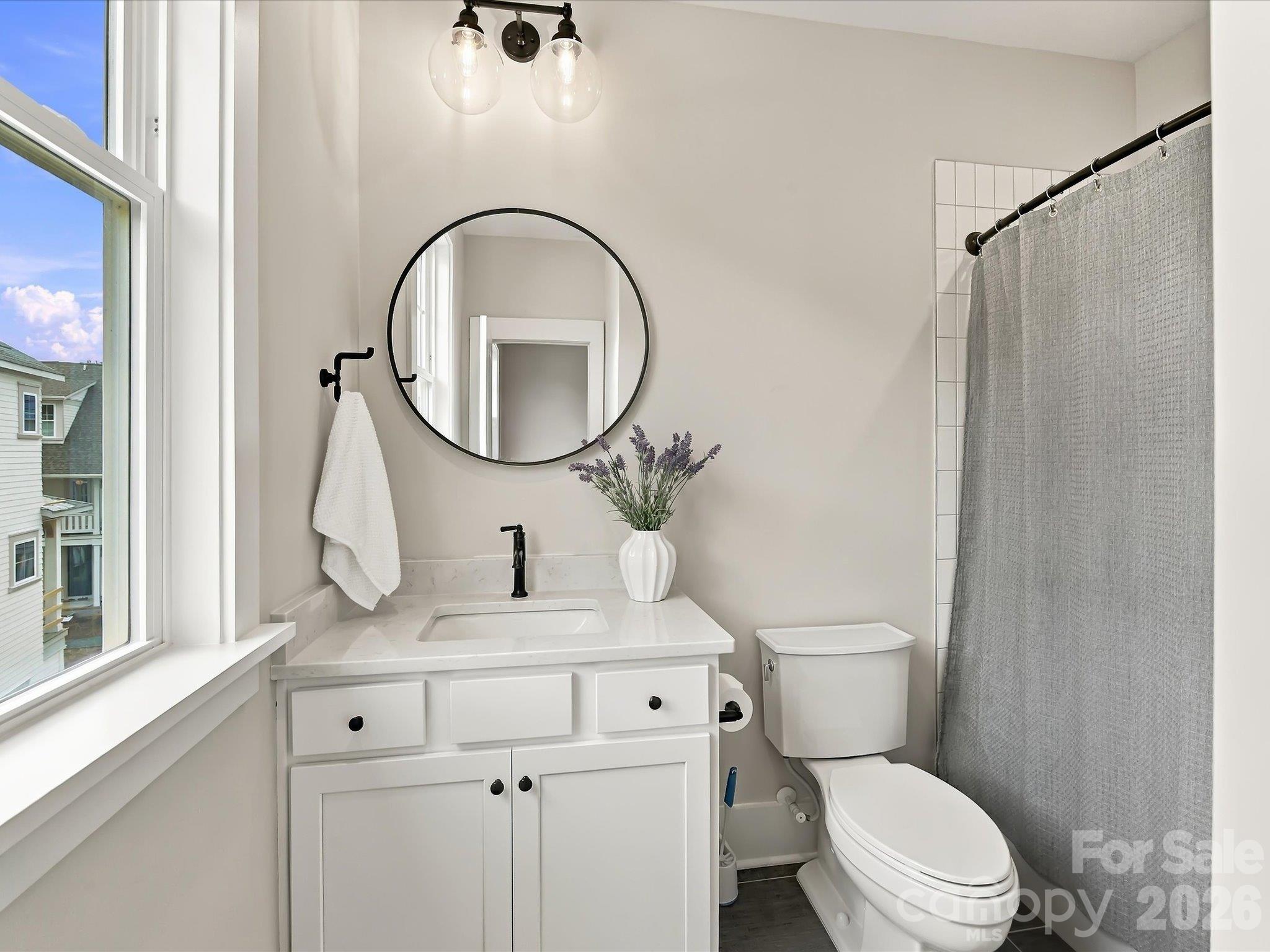 Bright second-bedroom ensuite bath featuring a white vanity, marble-look countertop, matte black fixtures, round mirror, and tub/shower combination. - 225 Davidson Gateway Drive, Davidson