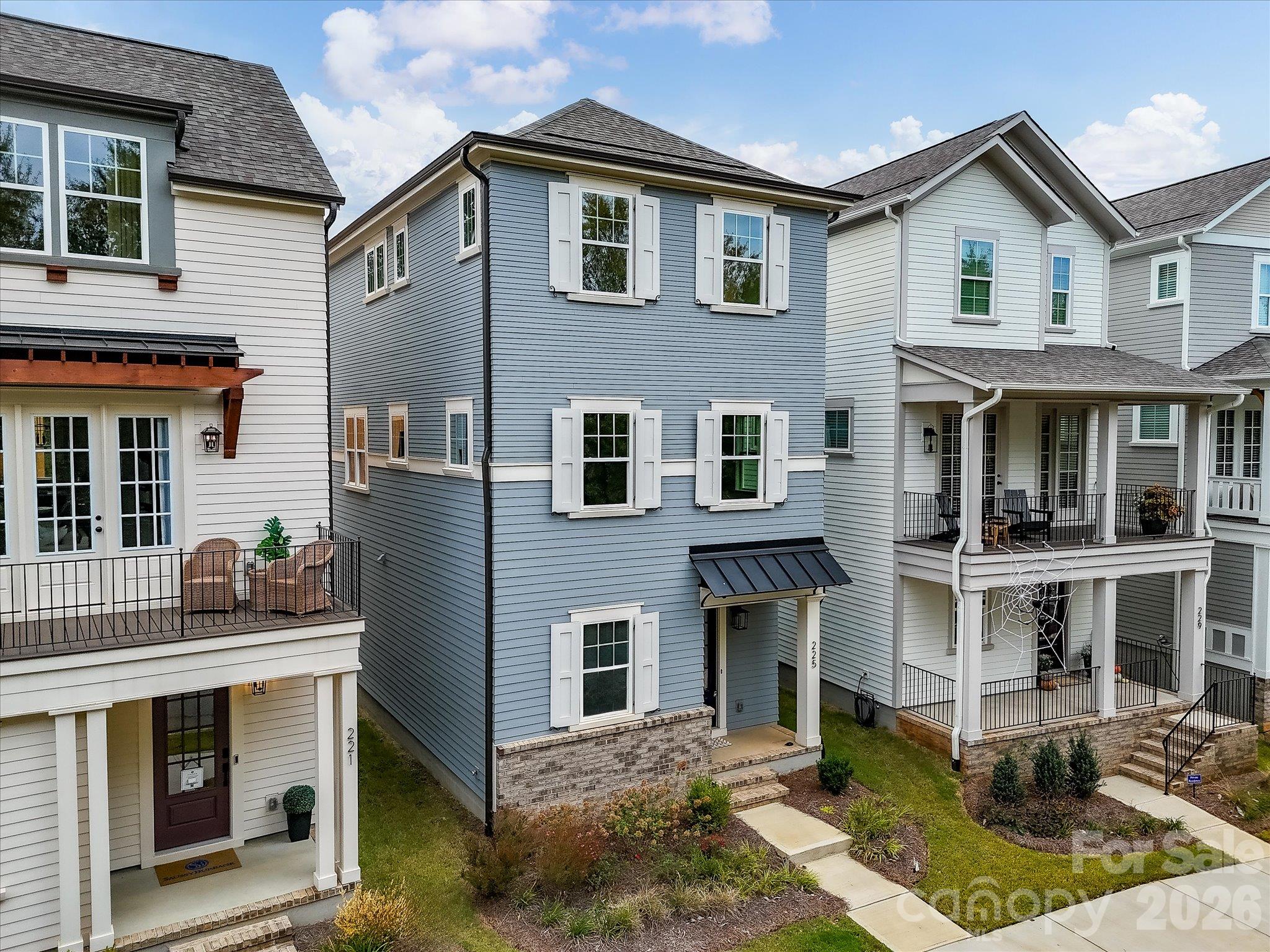Elevated drone view showcasing this charming three-story home with blue-gray siding, white shutters, stone accents, and attractive landscaping. - 225 Davidson Gateway Drive, Davidson