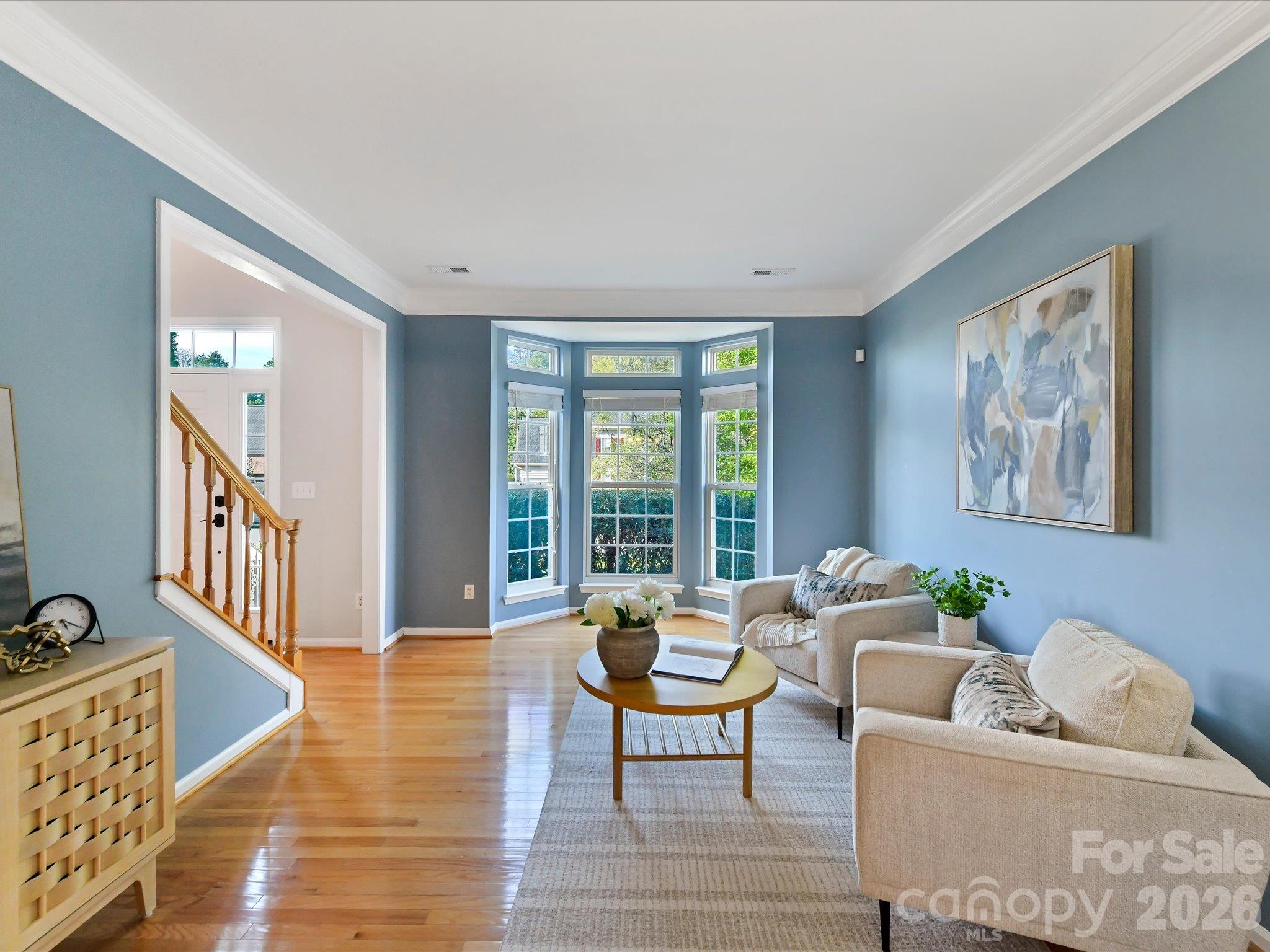 Inviting living room featuring beautiful hardwood floors, elegant crown molding and a sunlit bay window. - 3819 Waters Reach Lane, Indian Trail