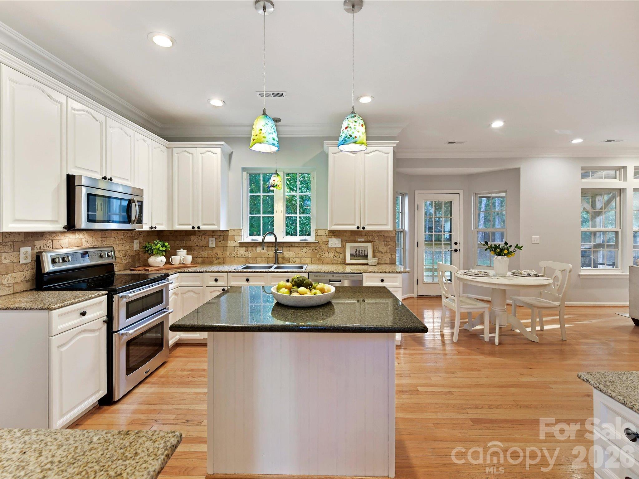 Spacious kitchen featuring modern white cabinetry, granite countertops, stainless steel appliances, a center island, and beautiful hardwood floors. - 3819 Waters Reach Lane, Indian Trail