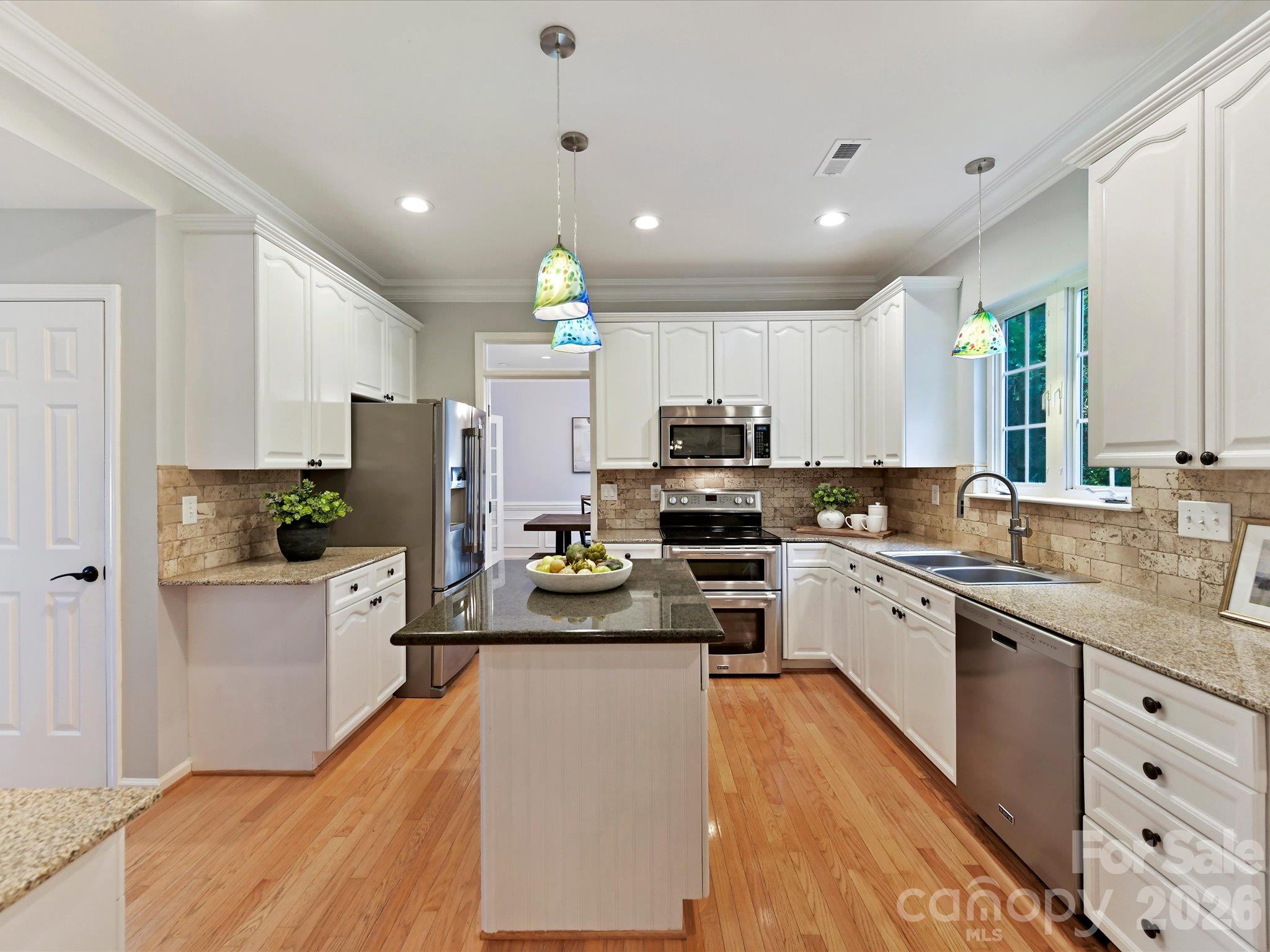 Spacious kitchen featuring modern white cabinetry, granite countertops, stainless steel appliances, a center island, and beautiful hardwood floors. - 3819 Waters Reach Lane, Indian Trail