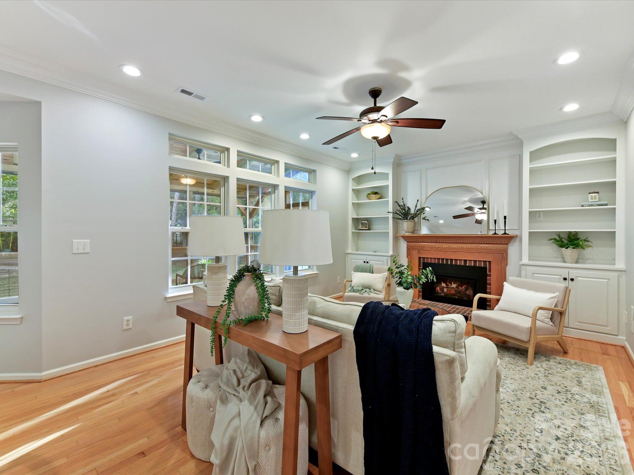 Inviting great room featuring a cozy fireplace, custom built-ins, beautiful hardwood floors, and expansive windows overlooking the backyard. - 3819 Waters Reach Lane, Indian Trail