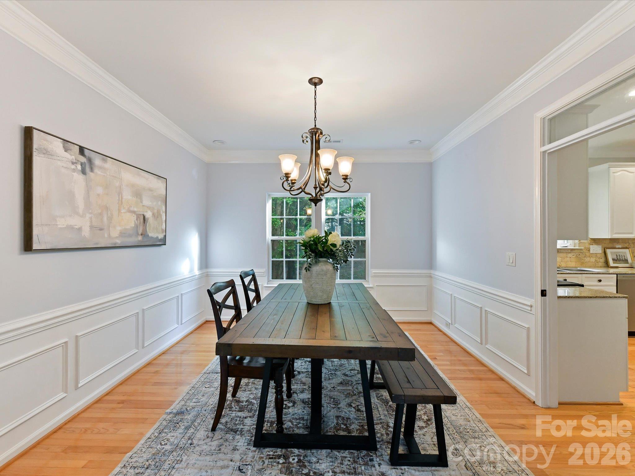 Elegant dining room featuring beautiful hardwood floors, classic wainscoting, crown molding, a decorative chandelier, and abundant natural light. - 3819 Waters Reach Lane, Indian Trail