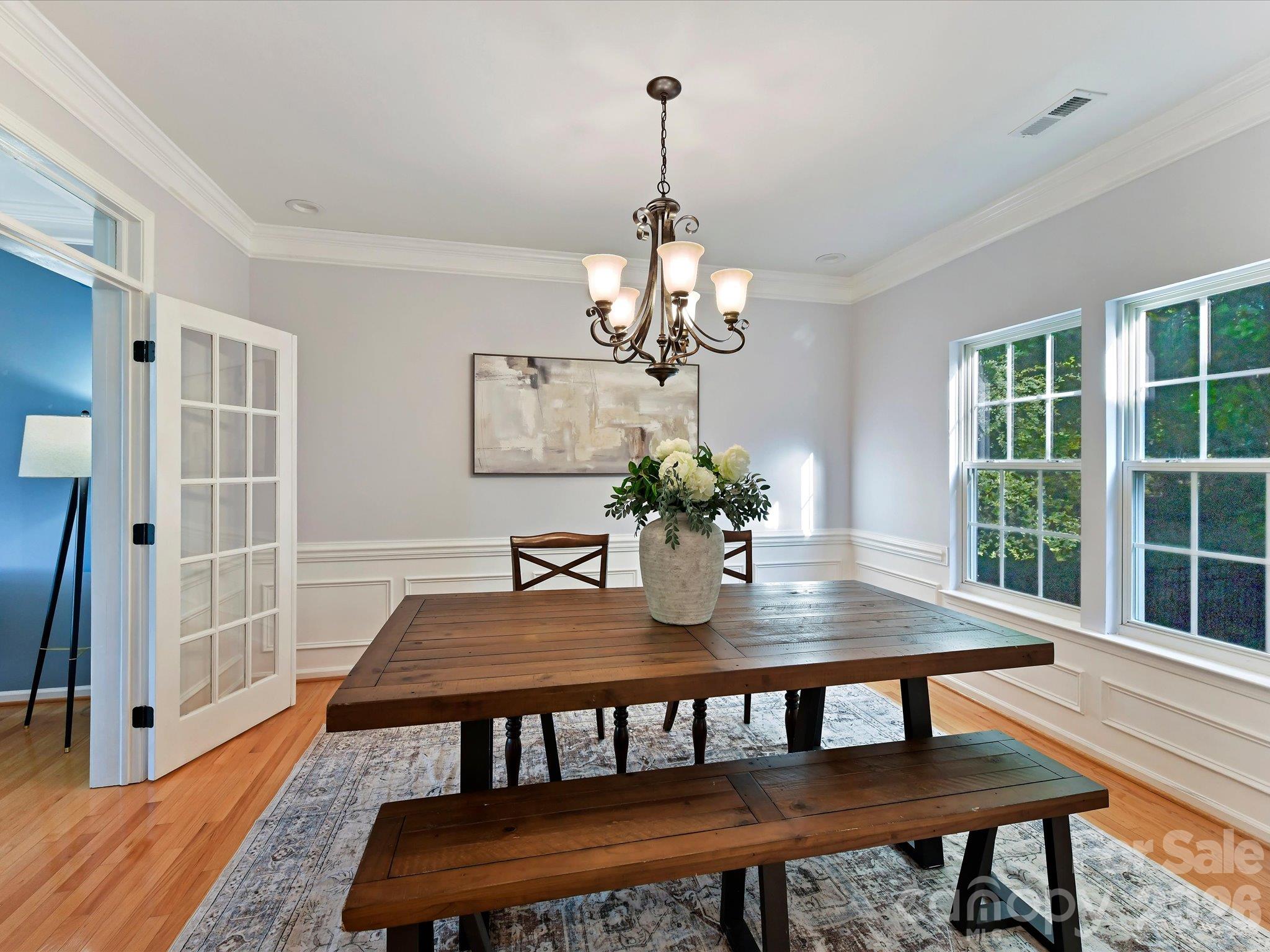 Elegant dining room featuring beautiful hardwood floors, classic wainscoting, crown molding, a decorative chandelier, and abundant natural light. - 3819 Waters Reach Lane, Indian Trail