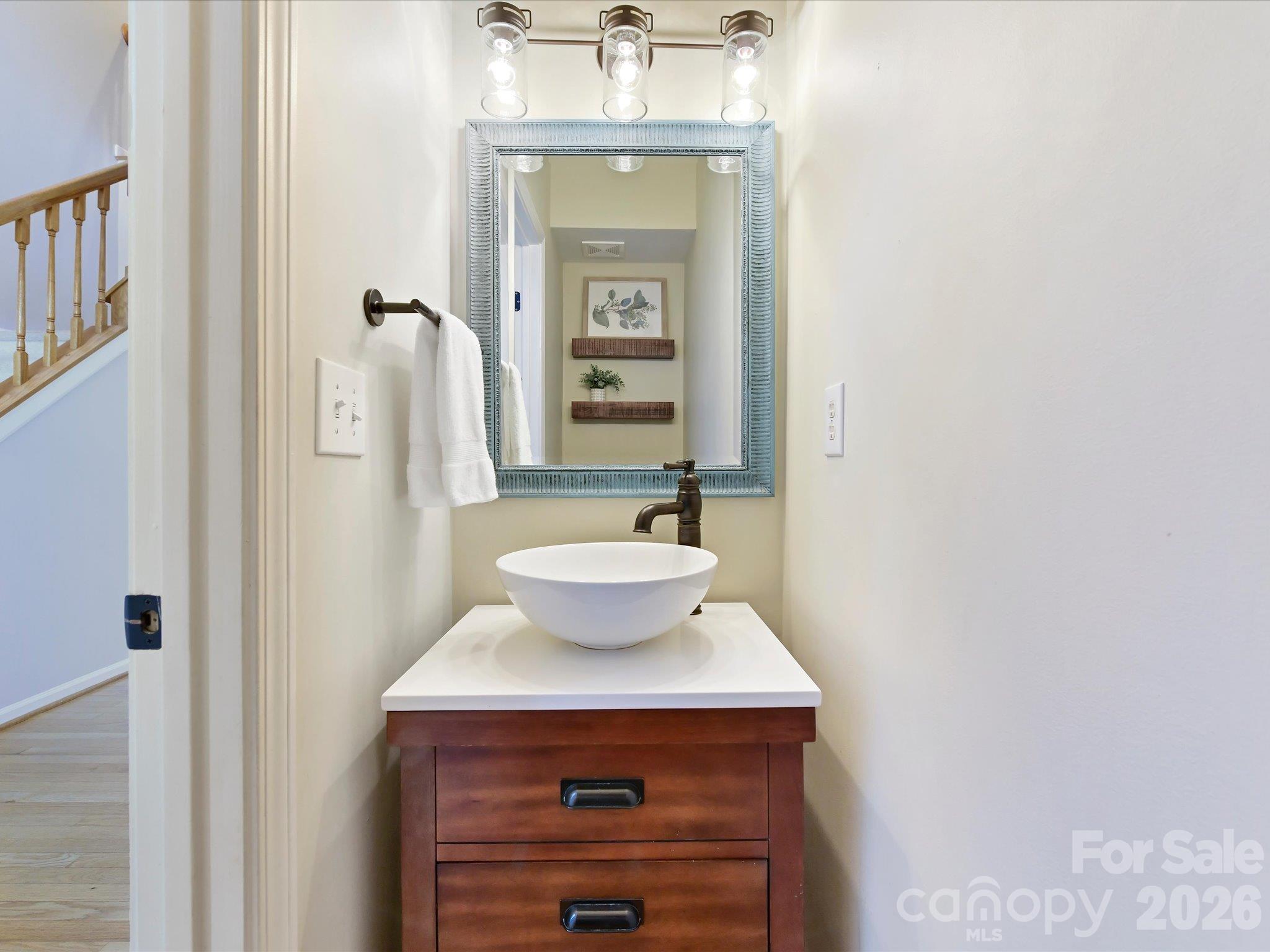 Stylish half bath featuring a modern vessel sink, rich wood vanity, decorative framed mirror, and contemporary lighting. - 3819 Waters Reach Lane, Indian Trail