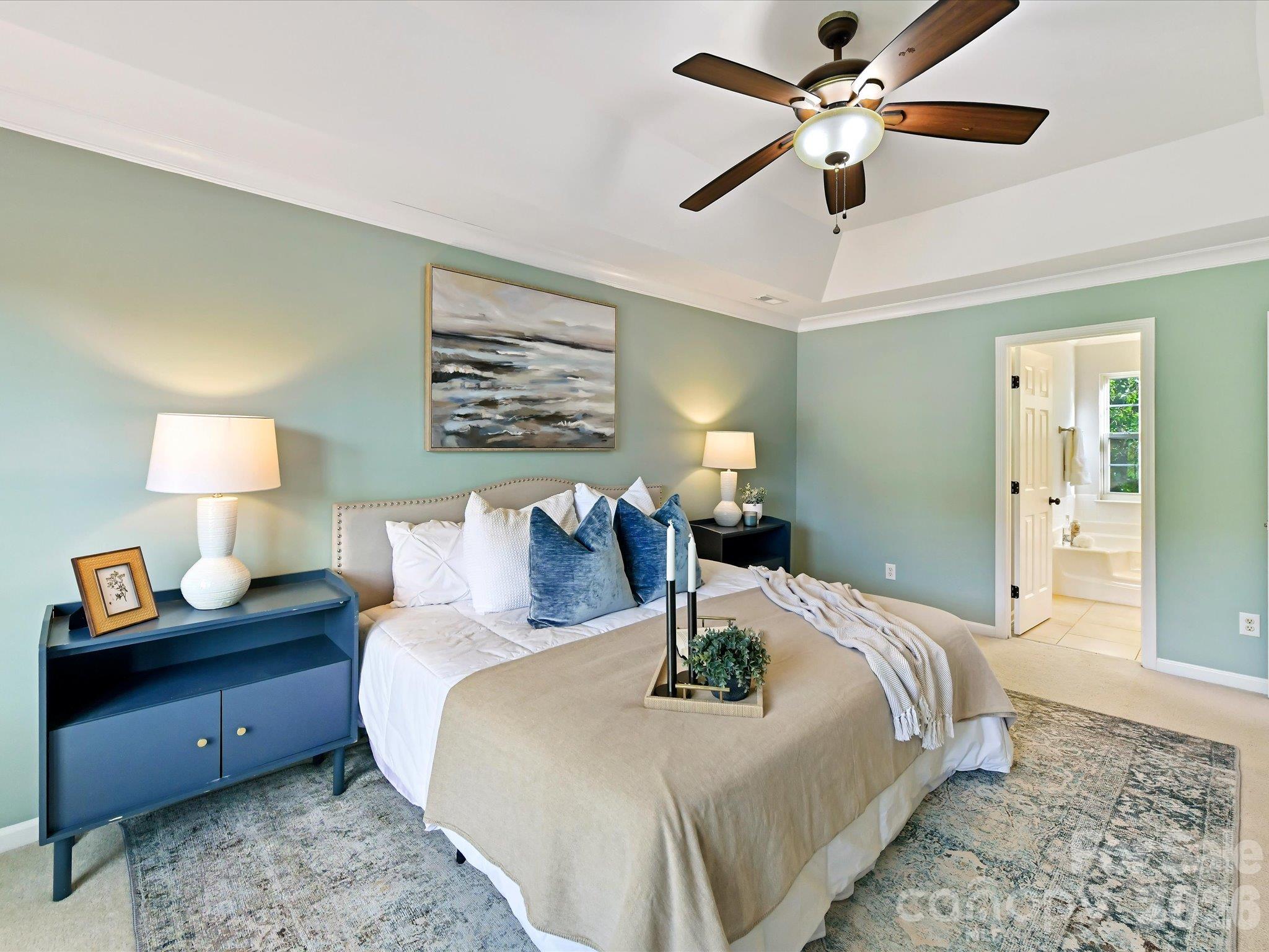 Spacious primary suite featuring a tray ceiling, soothing wall colors, abundant natural light, and a private ensuite bath. - 3819 Waters Reach Lane, Indian Trail