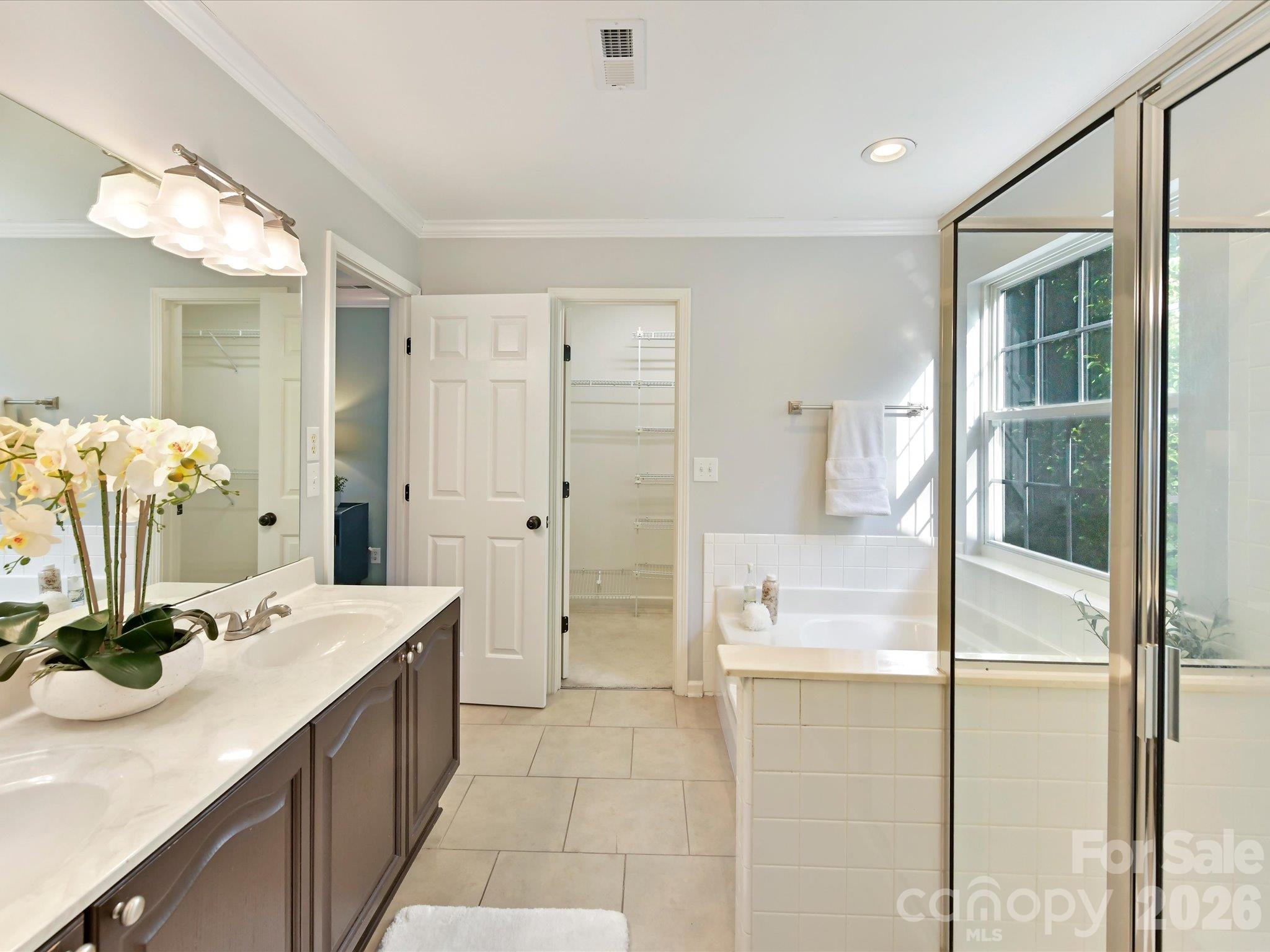Spacious primary bath featuring a dual-sink vanity, relaxing soaking tub, separate glass-enclosed shower, and abundant natural light. - 3819 Waters Reach Lane, Indian Trail
