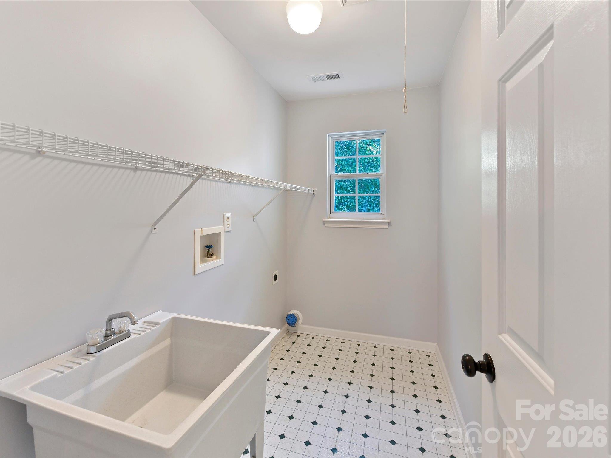 Convenient laundry room featuring a utility sink, overhead shelving, natural light, and ample space for laundry appliances. - 3819 Waters Reach Lane, Indian Trail