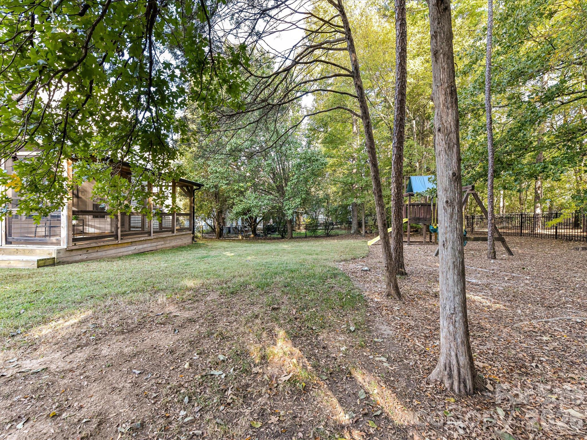 Spacious, tree-lined backyard featuring a fenced lawn, children's playset, and plenty of room for outdoor activities and relaxation. - 3819 Waters Reach Lane, Indian Trail