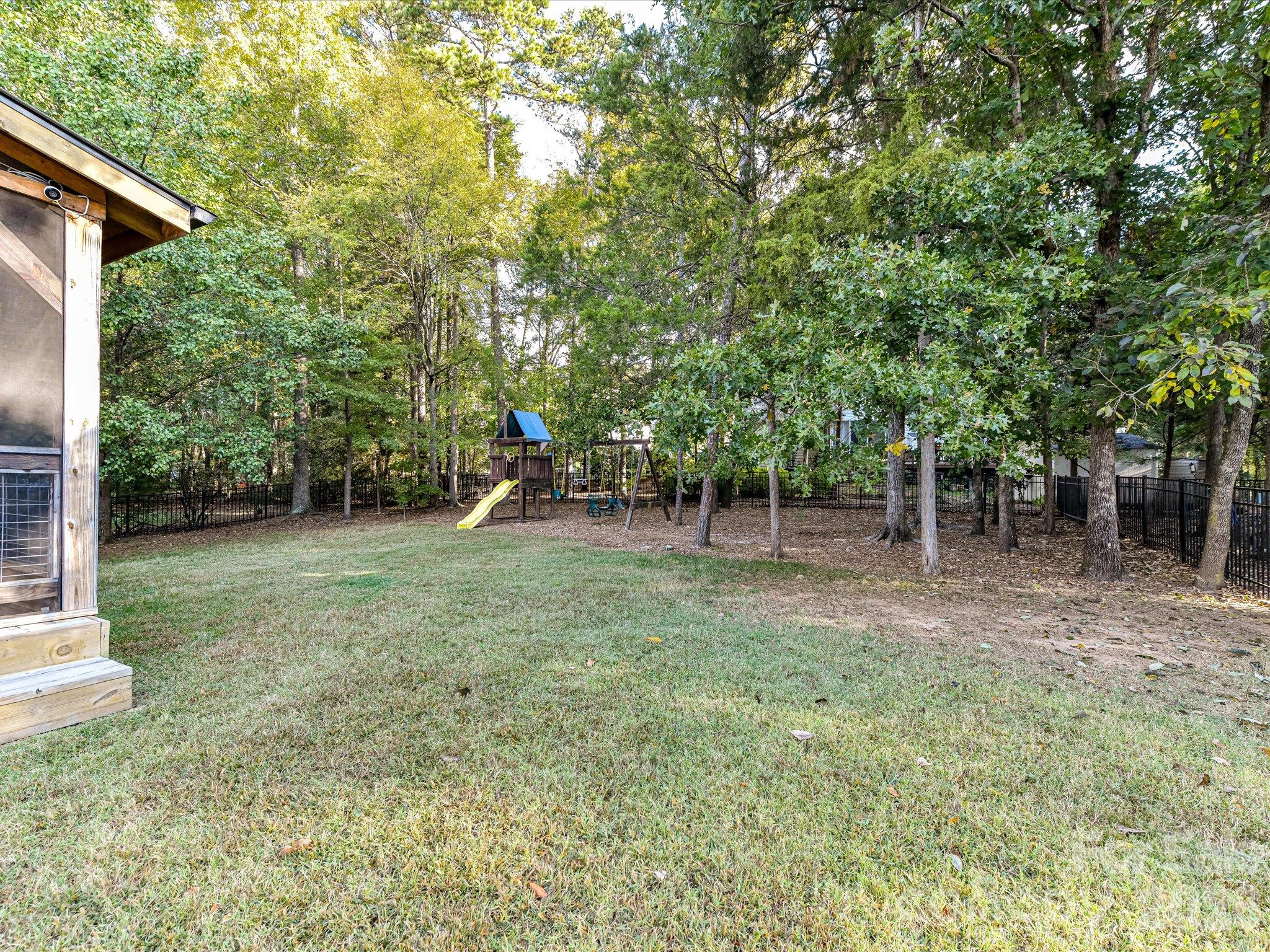 Spacious, tree-lined backyard featuring a fenced lawn, children's playset, and plenty of room for outdoor activities and relaxation. - 3819 Waters Reach Lane, Indian Trail