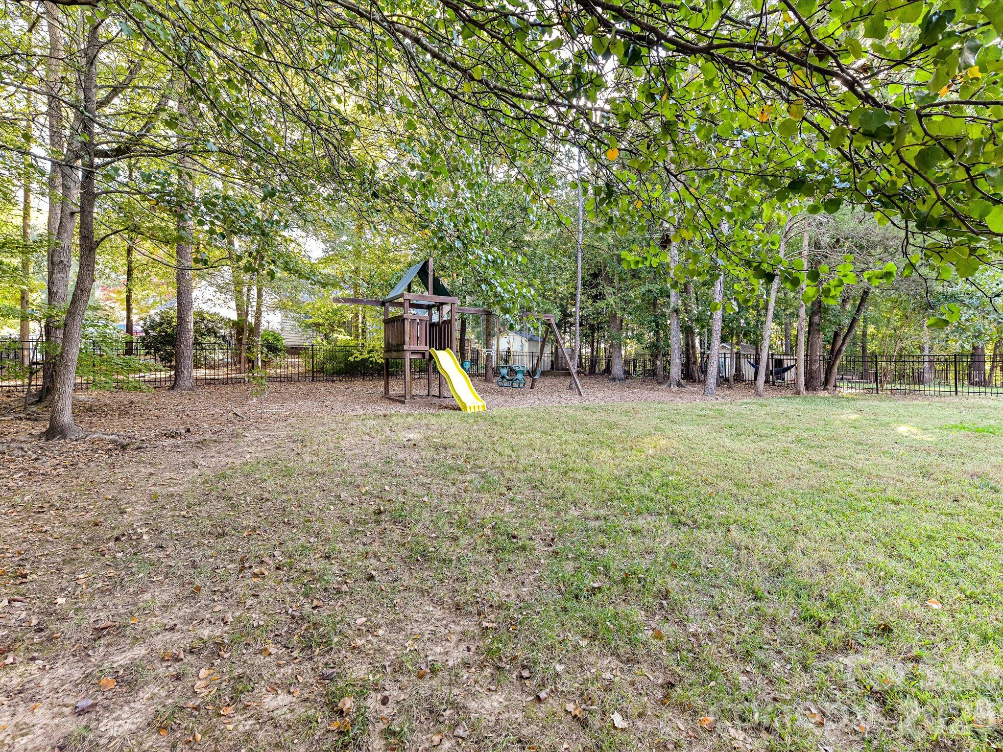 Spacious, tree-lined backyard featuring a fenced lawn, children's playset, and plenty of room for outdoor activities and relaxation. - 3819 Waters Reach Lane, Indian Trail