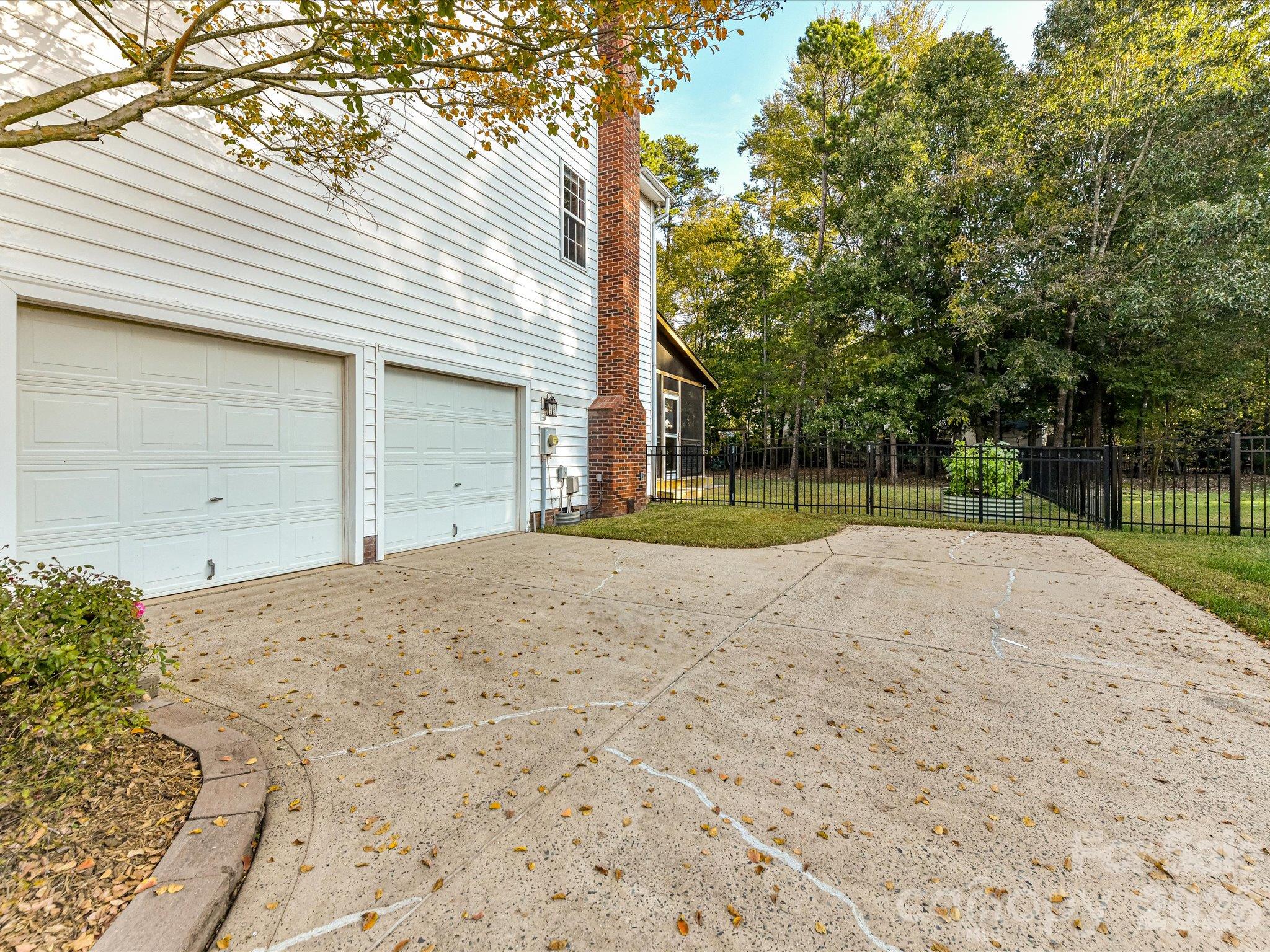 Spacious two-car garage featuring a wide concrete driveway, convenient side access, and a fenced backyard surrounded by mature trees. - 3819 Waters Reach Lane, Indian Trail