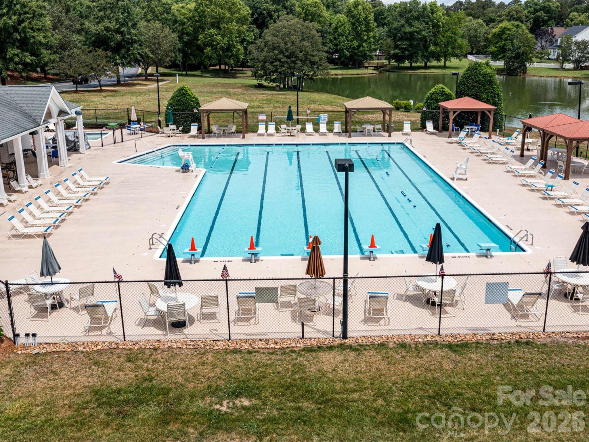 Brandon Oaks community pool featuring spacious swimming lanes, a relaxing poolside deck with lounge chairs and shaded cabanas, and scenic pond views. - 3819 Waters Reach Lane, Indian Trail