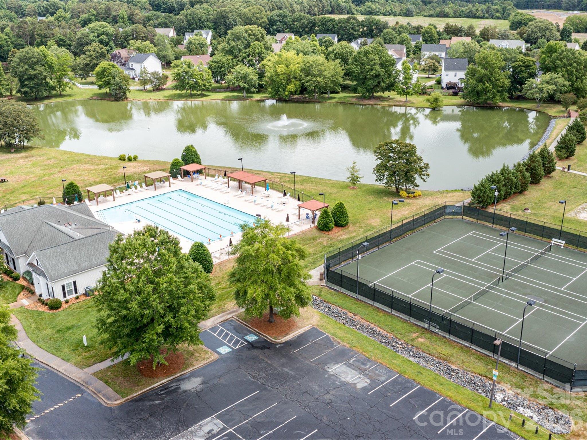 Aerial view of Brandon Oaks community amenities featuring a swimming pool, pickleball/tennis courts, basketball court, and scenic pond surrounded by lush greenery. - 3819 Waters Reach Lane, Indian Trail