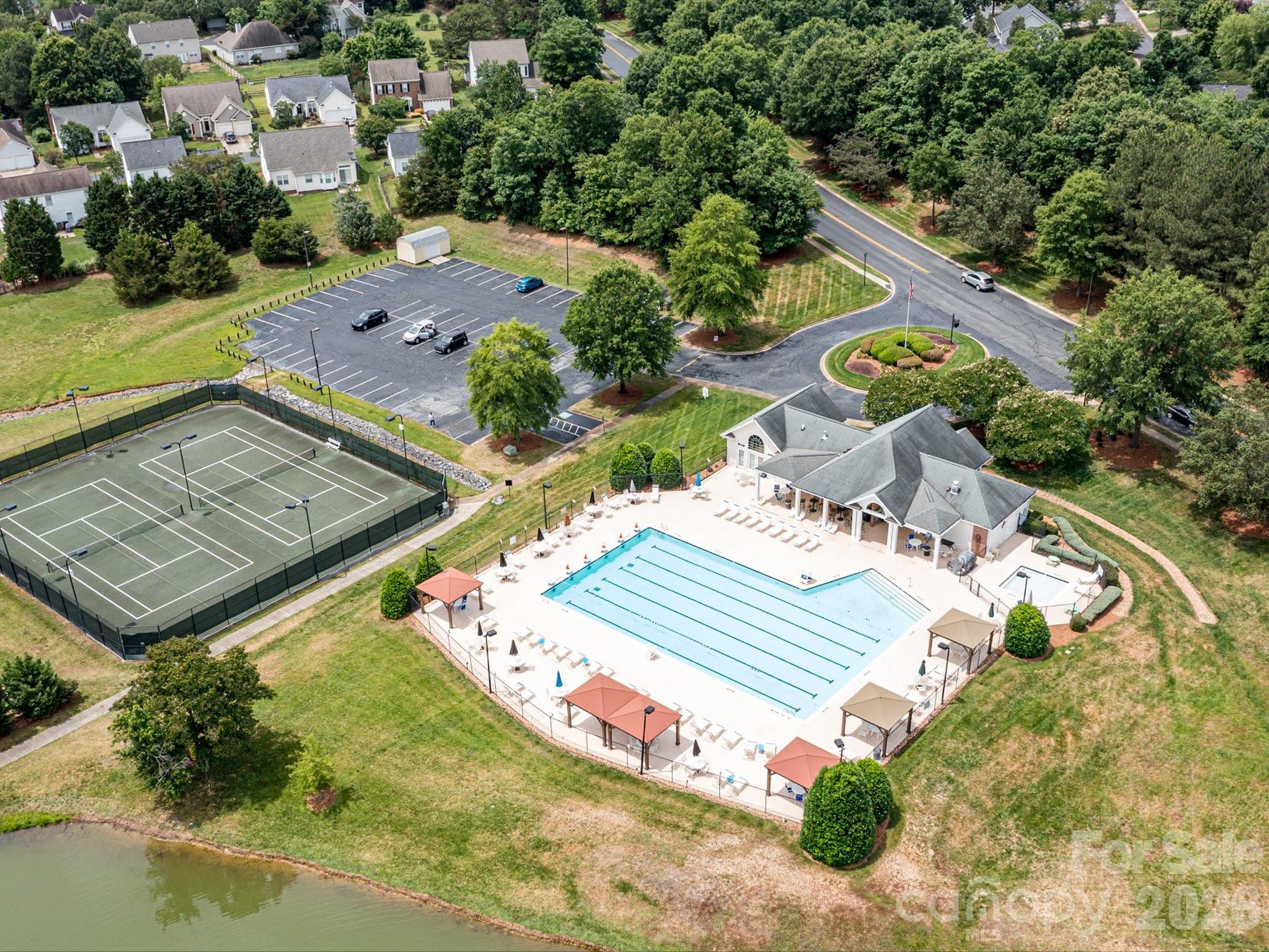 Aerial view of Brandon Oaks community amenities featuring a swimming pool, pickleball/tennis courts, basketball court, and scenic pond surrounded by lush greenery. - 3819 Waters Reach Lane, Indian Trail